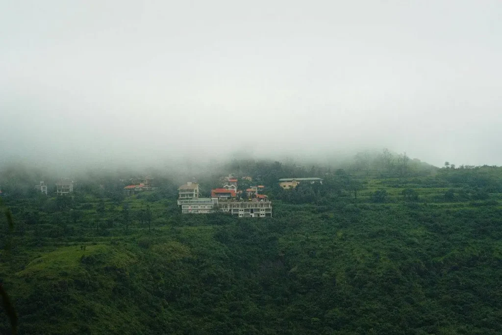 A scenic view of lush green hills and a resort nestled in the mist at Mahabaleshwar hill station near Mumbai and Pune.